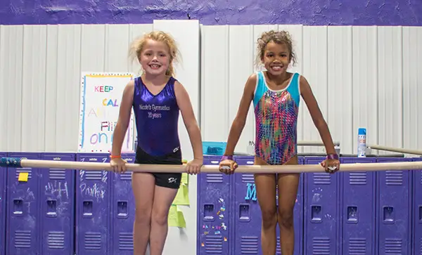 two young gymnasts smiling on the bar together